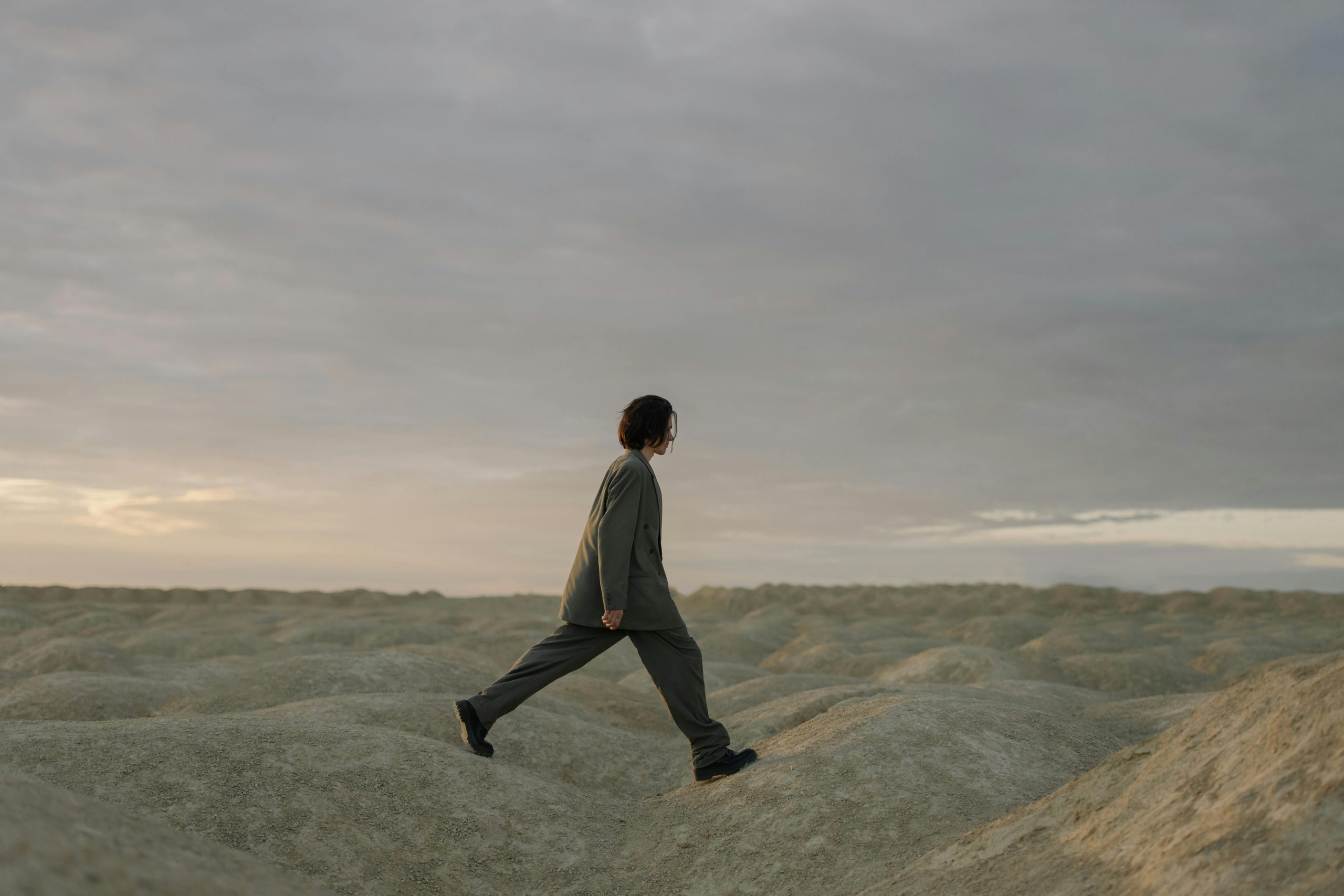 Man in white long sleeve shirt and black pants walking on gray sand